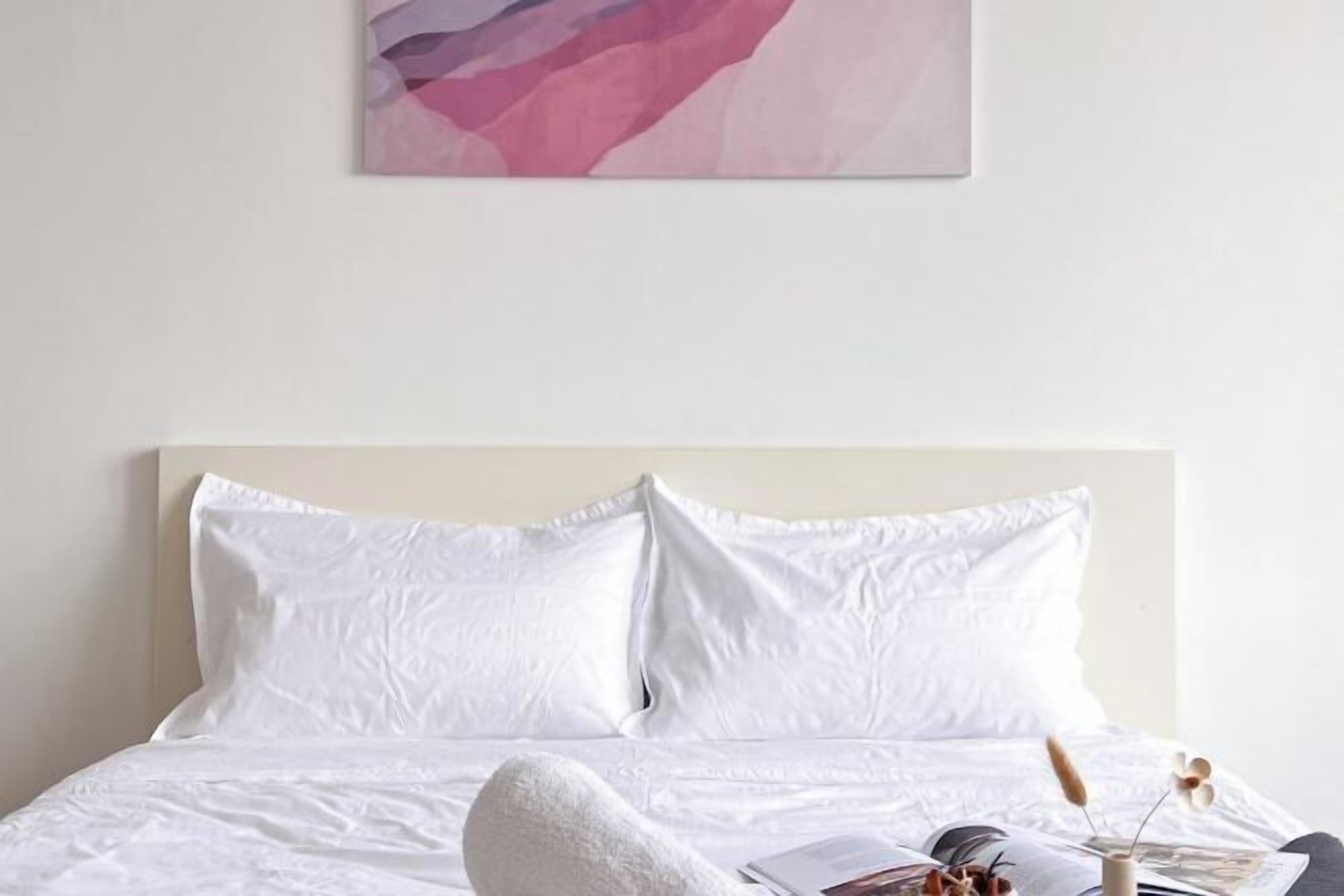 A bed with white bedding, a pillow, and a magazine on the side.