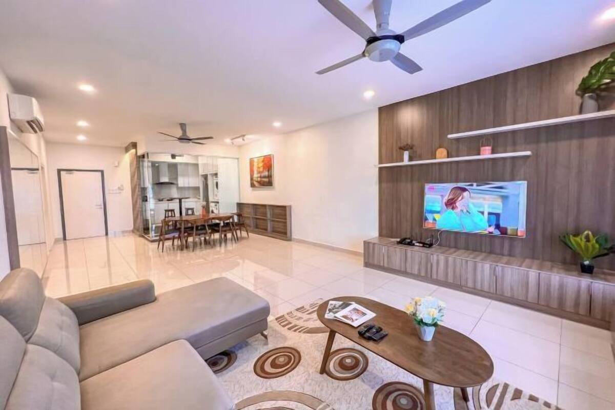 Ein modernes Wohnzimmer mit Sofa, Couchtisch und Fernseher. Im Hintergrund befindet sich ein Essbereich.