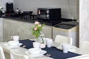 A dining area with a table set for two, white cups, bowls, and cutlery, a vase with flowers, and a microwave in the background. - Da Men Subang Jaya USJ by Iconique (Subang Jaya)