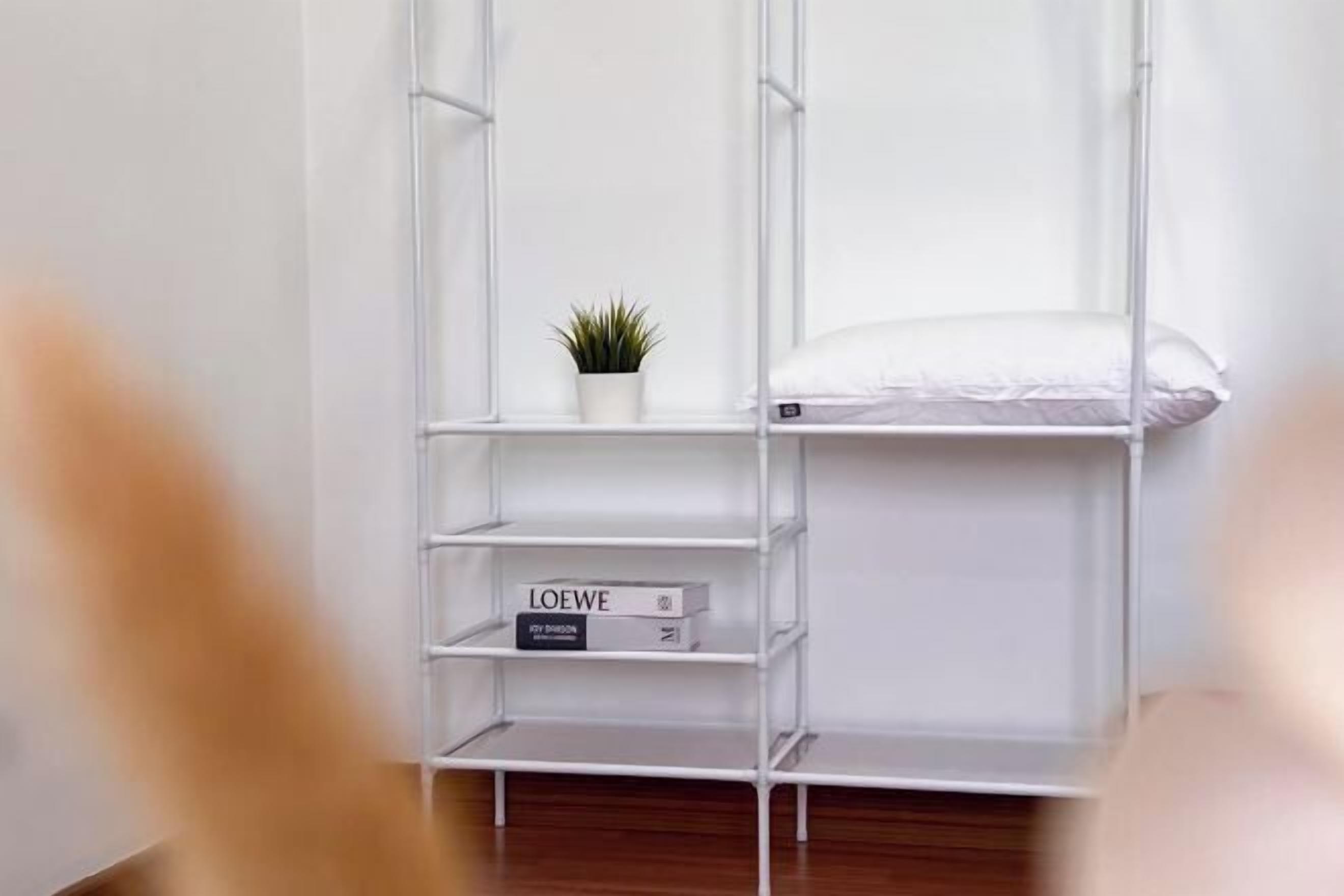 A white metal shelving unit with a small potted plant and a book titled 'LOEWE'.