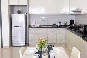 A modern kitchen with white cabinets, a stainless steel refrigerator, and a dining area with a table set for four. - Da Men Subang Jaya USJ by Iconique (Subang Jaya)
