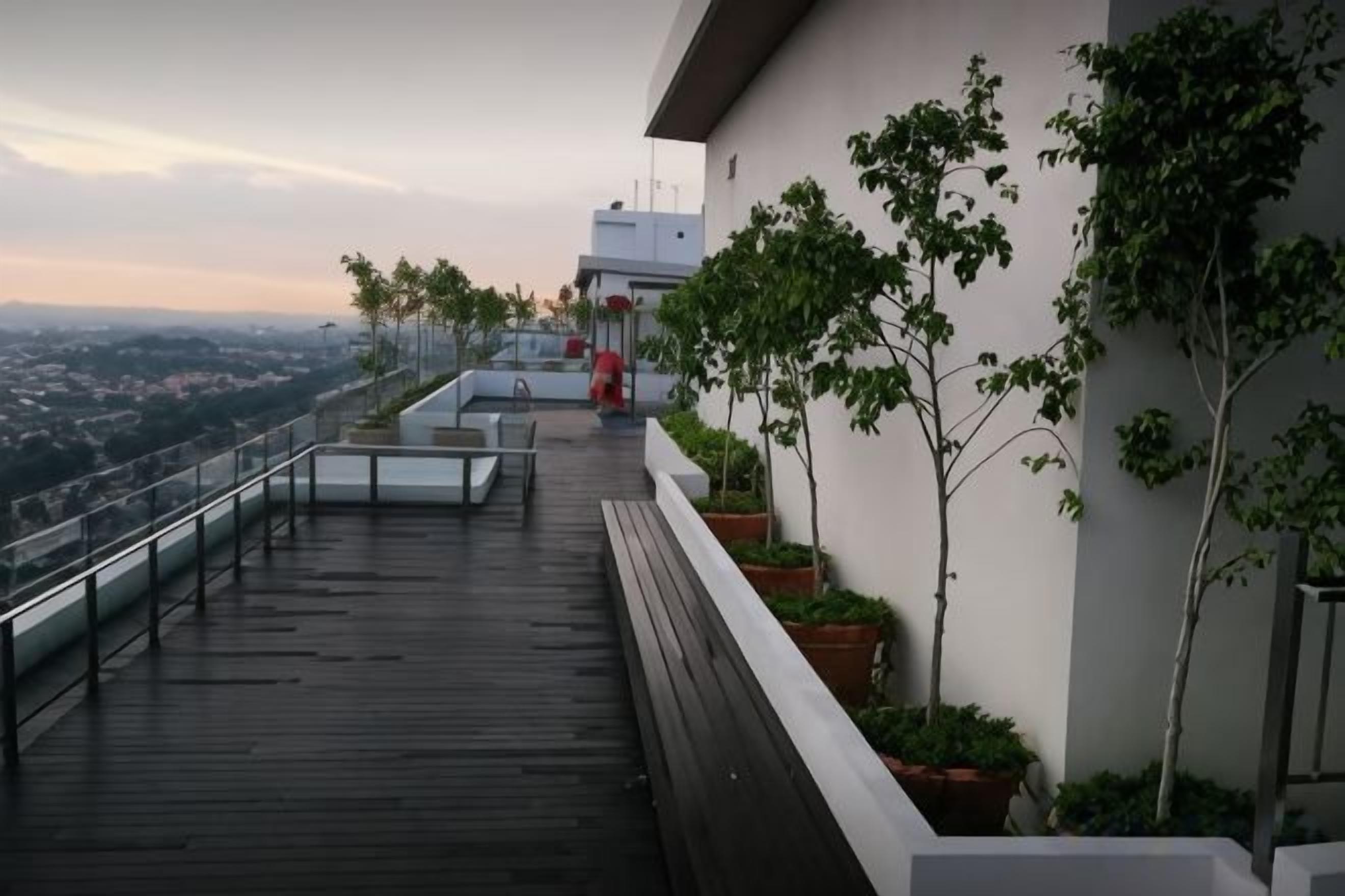 A rooftop terrace with a wooden deck, potted plants, and a view of the city.