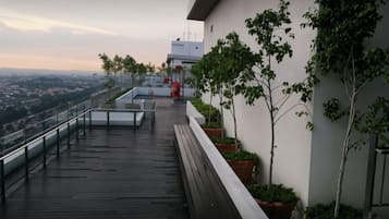 A rooftop terrace with a wooden deck, potted plants, and a view of the city.