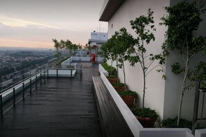 Una terraza en la azotea con piso de madera, plantas en macetas y vista de la ciudad.