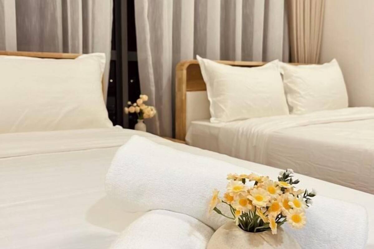 Ein Hotelzimmer mit zwei Betten, weißer Bettwäsche und einem Blumenstrauß mit gelben Blumen auf dem Bett.