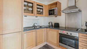 A compact kitchen with wooden cabinets, a stainless steel microwave, a Bosch oven, and a sink. - Sleek Southwark 2BR, Furniture & Decor Included, by Blueground (London)