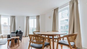 A modern living room with a round wooden table and four chairs, a grey sofa, and a small wooden stool. - Sleek Southwark 2BR, Furniture & Decor Included, by Blueground (London)