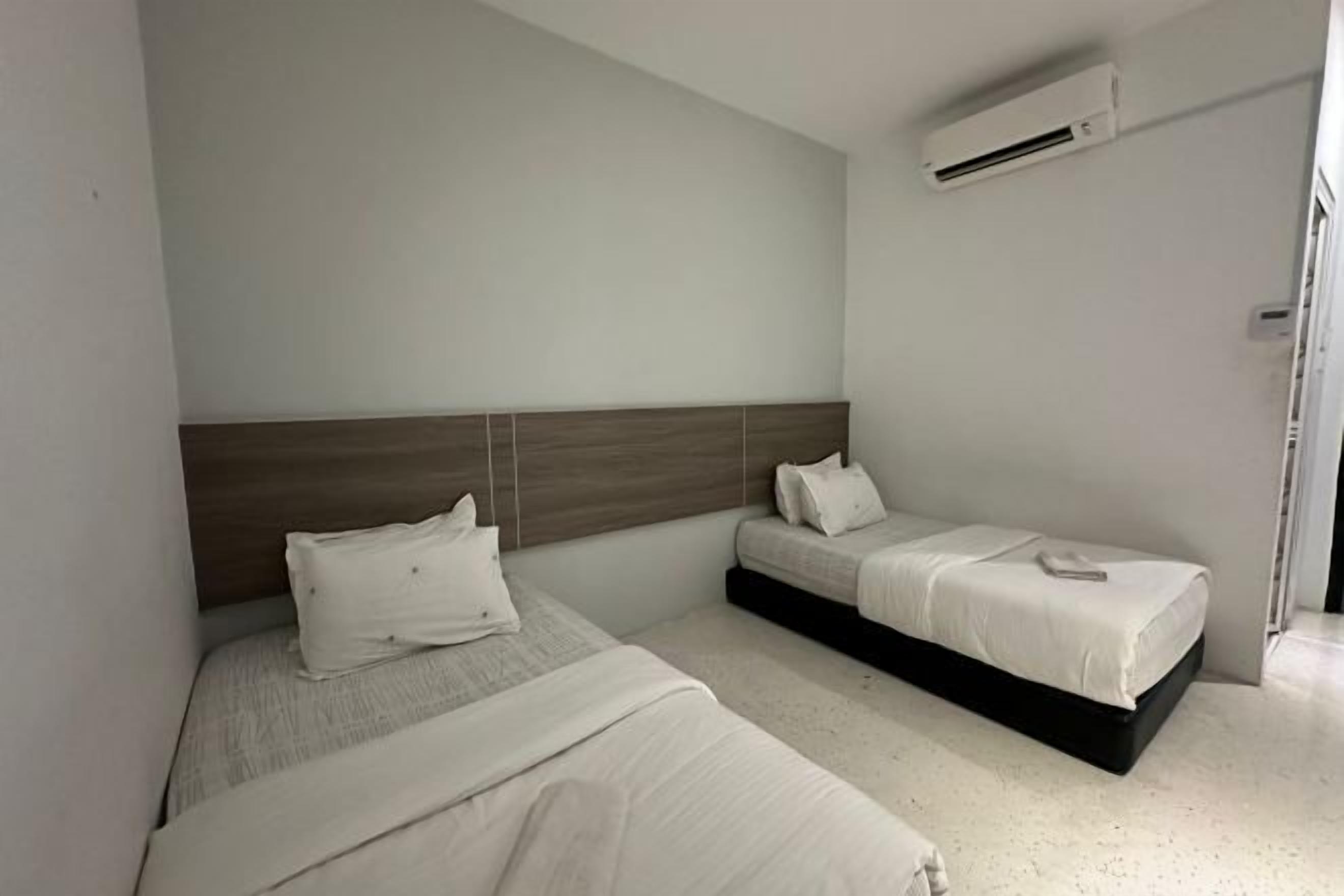 Una camera da letto con due letti, una testiera in legno e un condizionatore d'aria bianco.