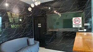 Un hall d’hôtel moderne avec un mur en marbre noir, un grand écran de télévision, un canapé et une table en bois.