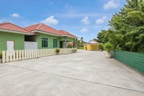 A residential area with a paved driveway, a white picket fence, and a green building with a red roof. - Collection O Langkawi near pantai cenang formerly tokman inn (Langkawi)