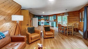 A cozy cabin interior with a living area, wooden walls, a kitchenette, and a dining table.