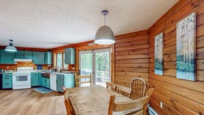 A cabin-style kitchen with wooden walls, teal cabinets, and a wooden dining table with chairs.