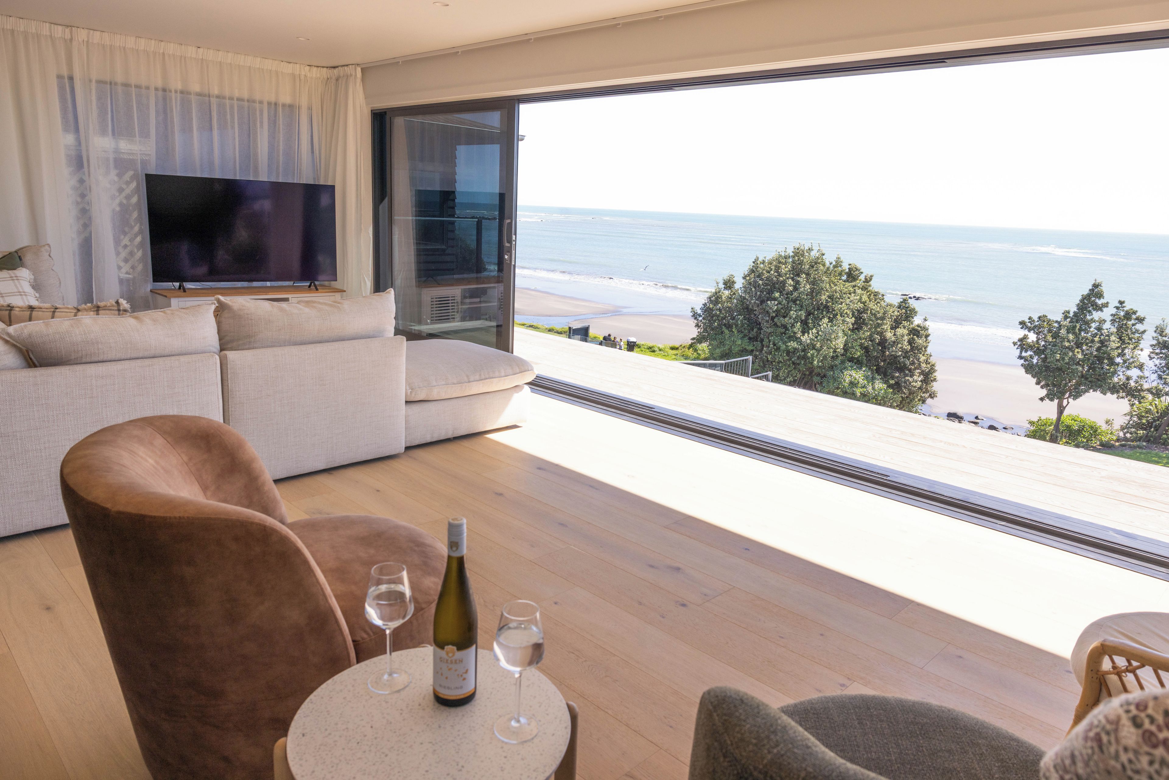 Een moderne woonkamer met een grote televisie, een bank en een tafel met een wijnfles en glazen.