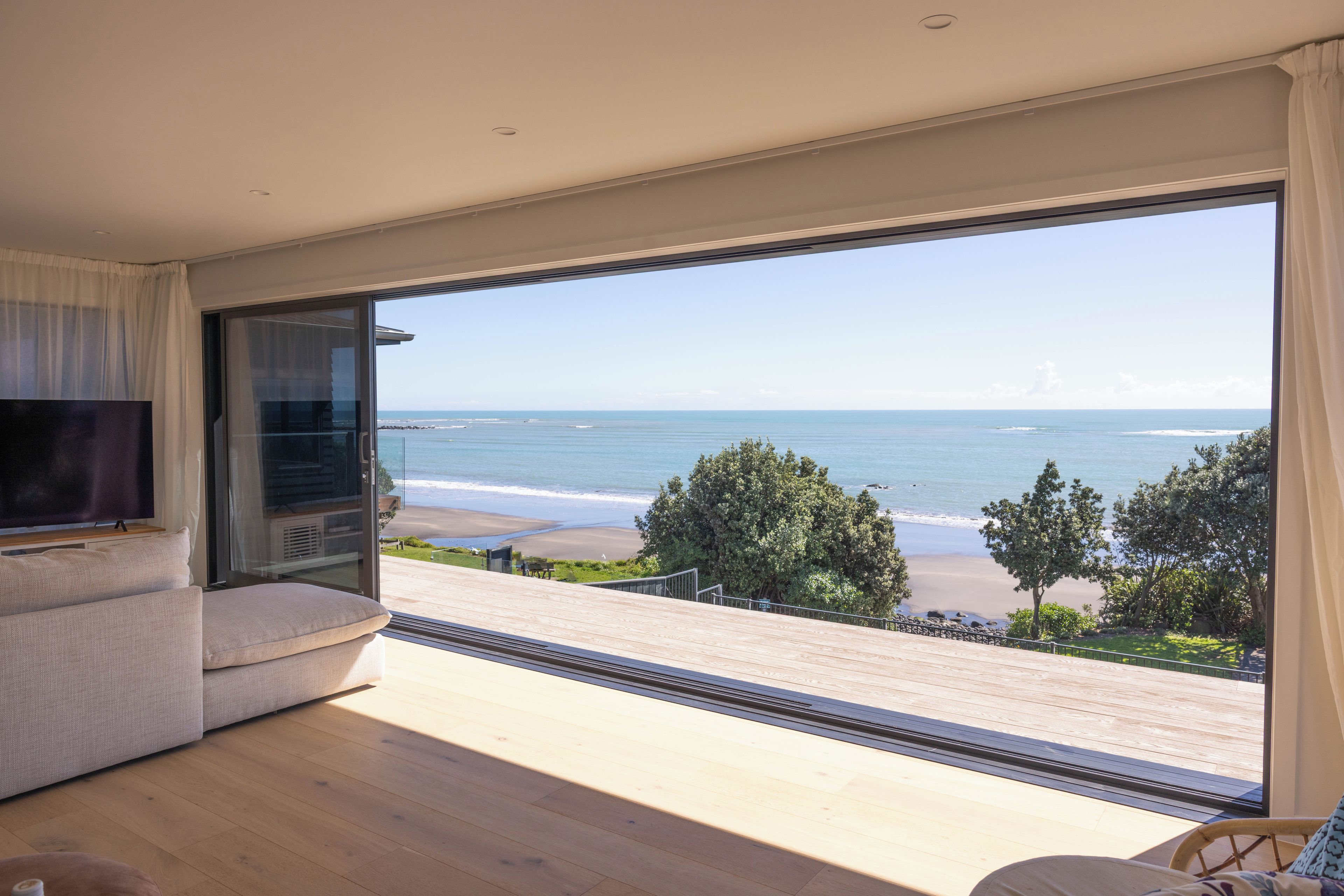 A modern living room with a large sliding glass door leading to a balcony overlooking a beach.