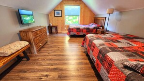 A bedroom with two beds, wooden flooring, a dresser, a TV, and a window with a view of greenery. - Catchin Crickets near Pictured Rocks and ATV Trails!  (Shingleton)