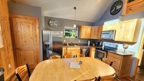 A kitchen with wooden cabinets, stainless steel appliances, and a round wooden table with chairs. - Catchin Crickets near Pictured Rocks and ATV Trails!  (Shingleton)