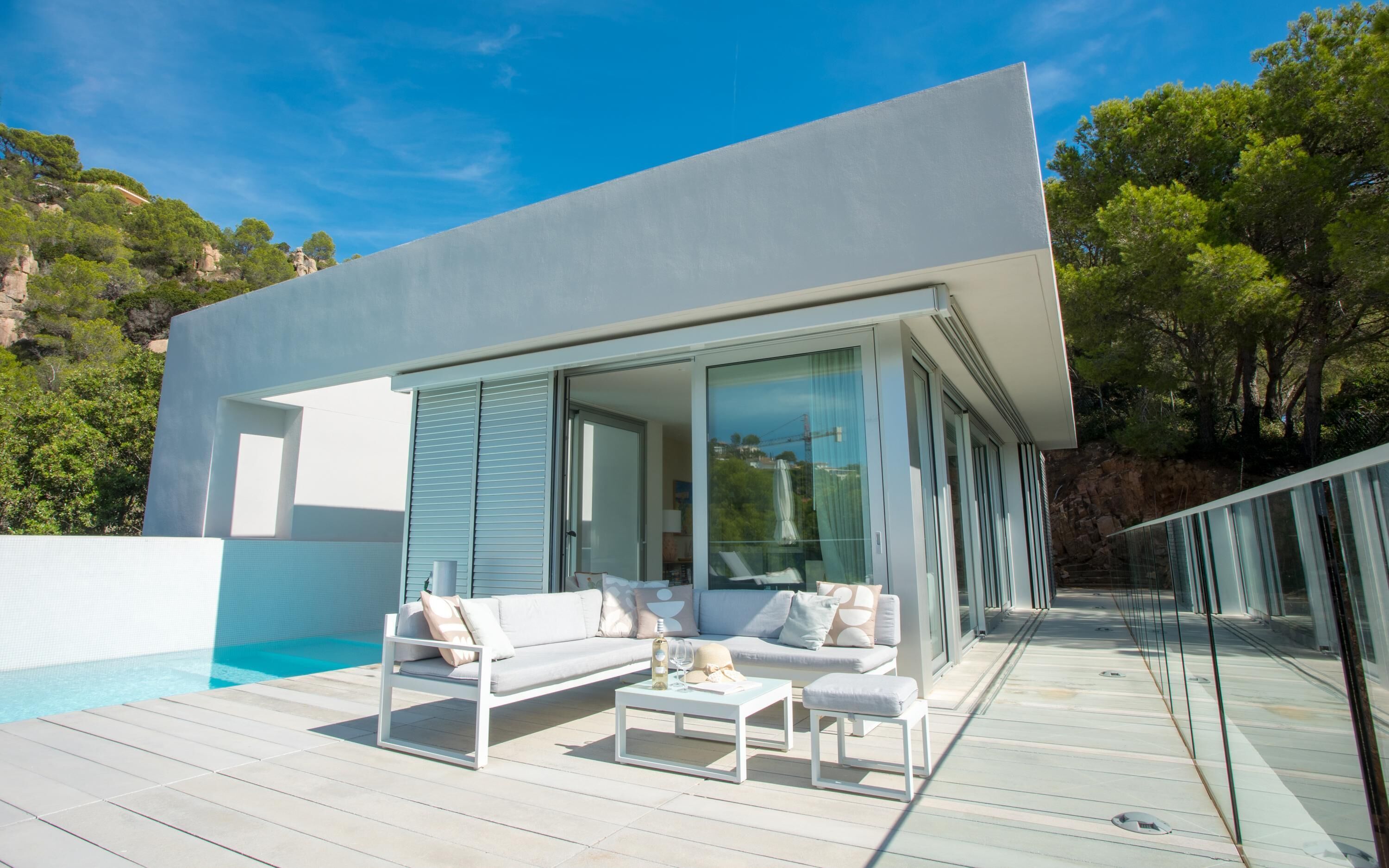A modern house with a pool, outdoor furniture, and a glass door leading to a deck.