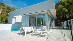 Ein modernes Haus mit Pool, Gartenmöbeln und einer Glastür, die auf eine Terrasse führt.