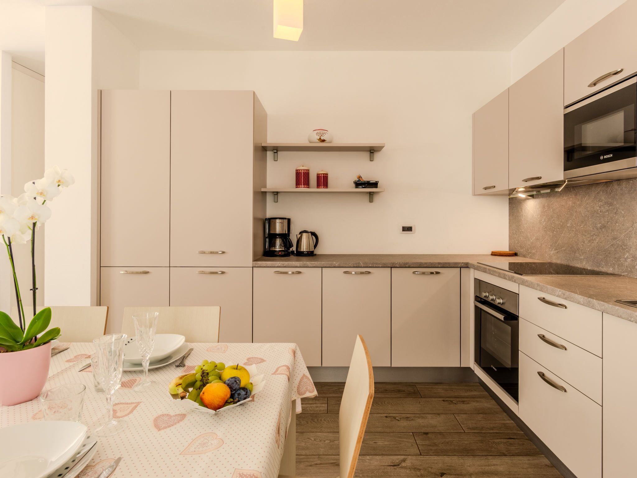 Una cocina moderna con armarios blancos, un horno Bosch y un comedor con una mesa para dos.