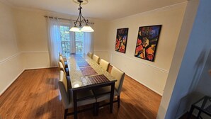 A dining room with a long table, chairs, a chandelier, and two abstract paintings on the wall. - Spacious and Family Friendly 6-bedrooms house in delightful Silver Spring. (Silver Spring)