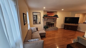 A living room with a fireplace, a sofa, a television, and wooden flooring. - Spacious and Family Friendly 6-bedrooms house in delightful Silver Spring. (Silver Spring)