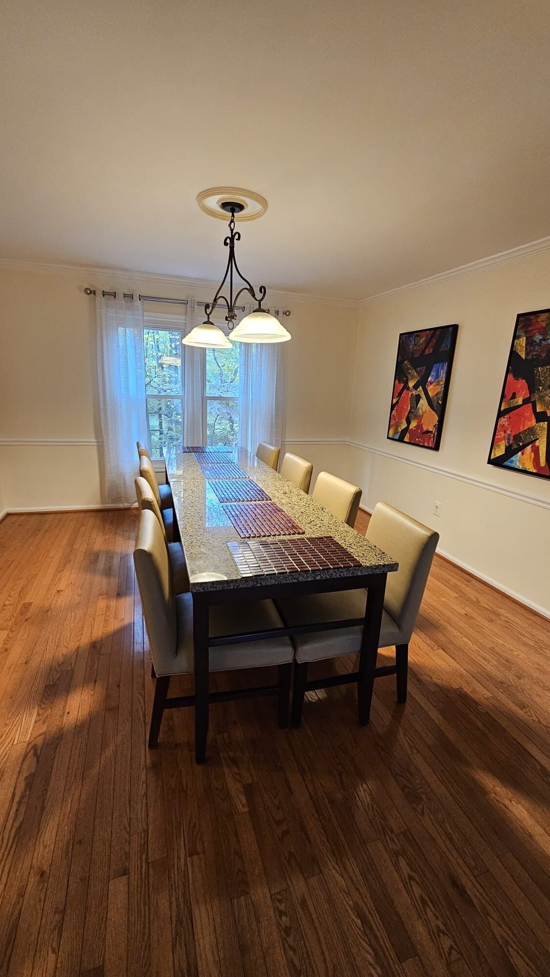 A dining room with a long table, chairs, a chandelier, and artwork on the walls.