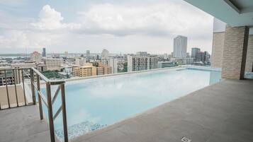 Piscina en la azotea con vistas a la ciudad, rodeada de edificios y un cielo despejado.