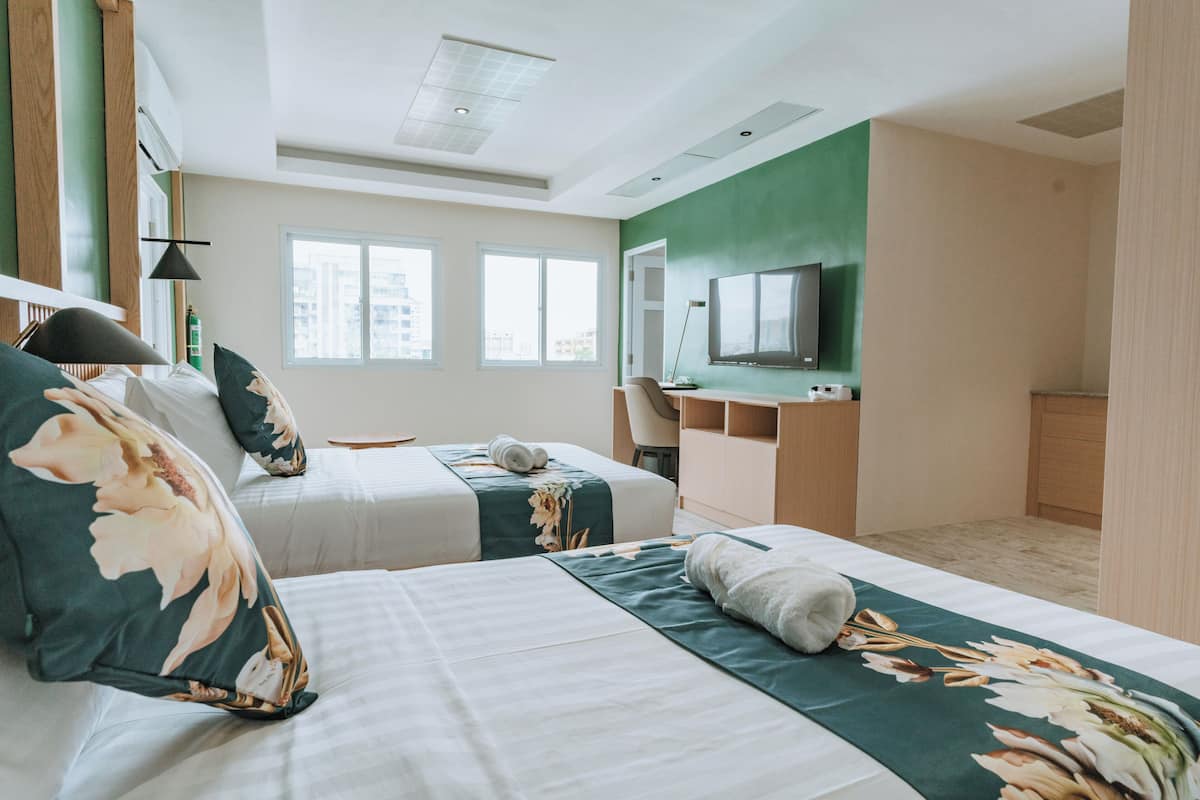 Habitación de hotel con dos camas, un escritorio, una silla, un televisor y ventanas amplias.