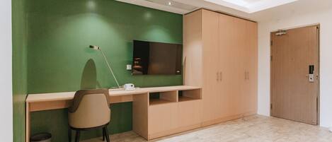 A modern room with a green accent wall, a wooden desk, a chair, a television, and a wardrobe.