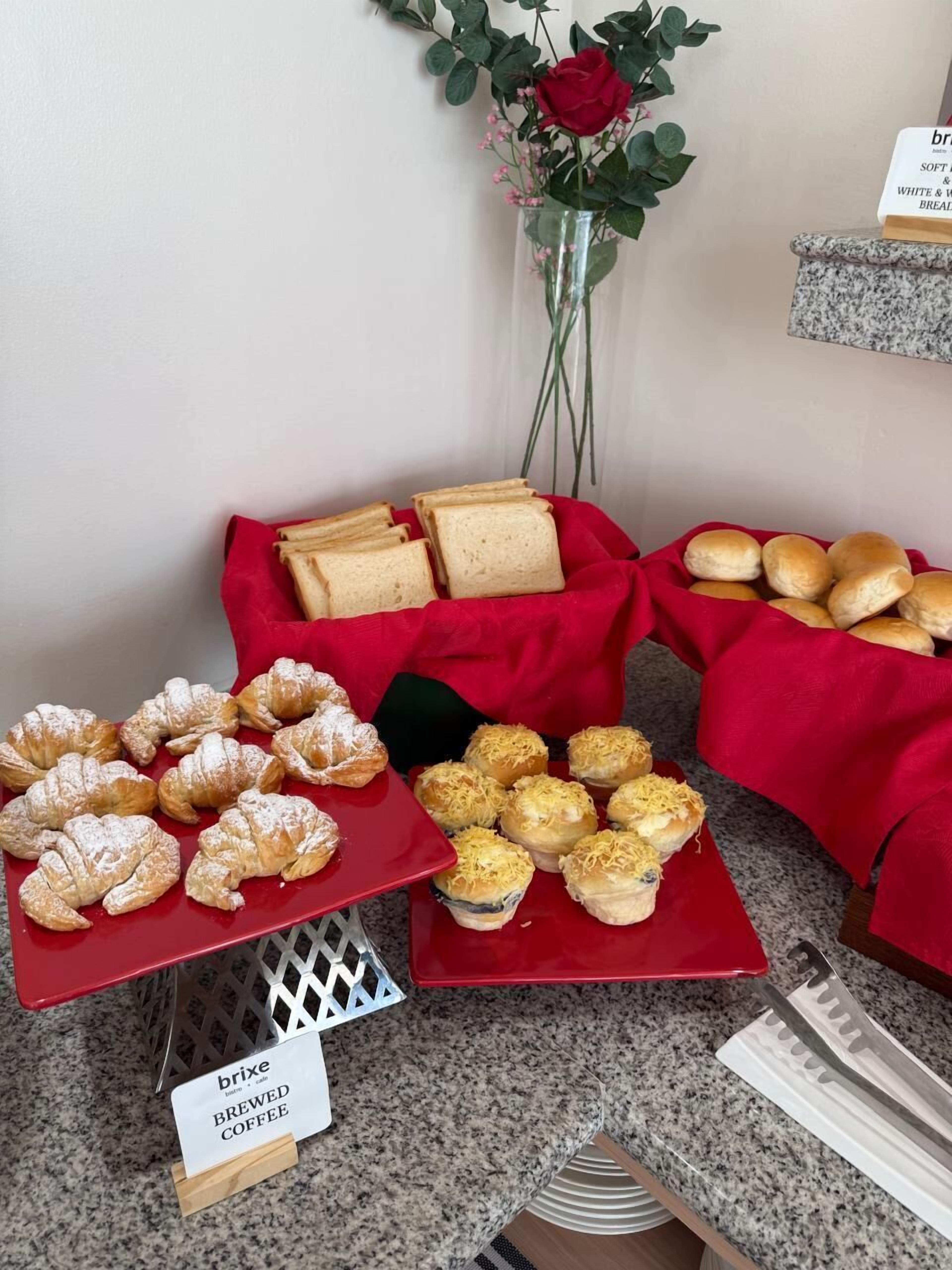 A buffet table with various baked goods, including croissants and bread rolls, and a sign indicating brewed coffee.