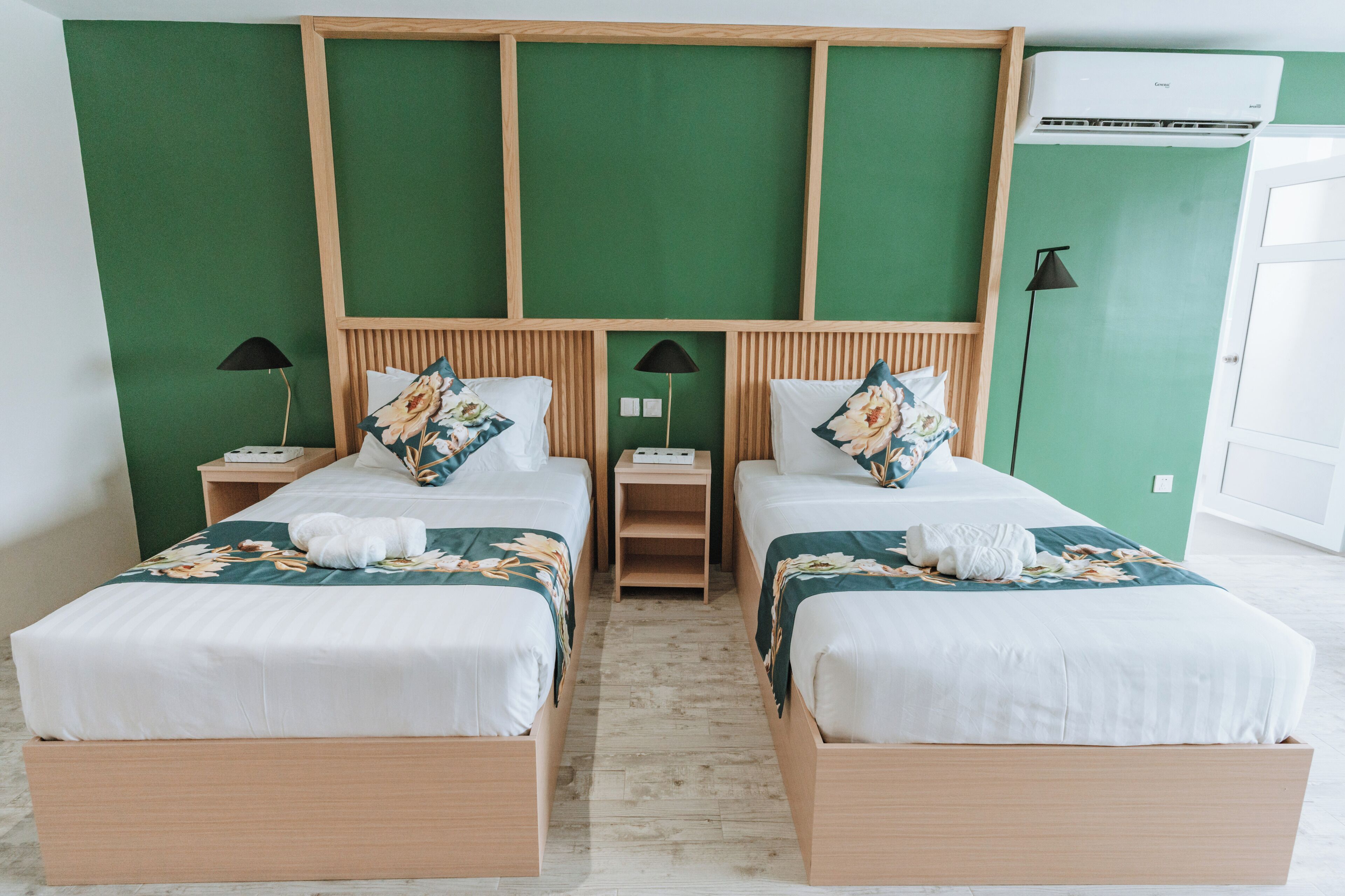 A hotel room with two beds, green walls, wooden headboard, and a white air conditioning unit.