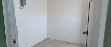 A bathroom with white tiled walls and floor, a visible electrical box, and a door frame.