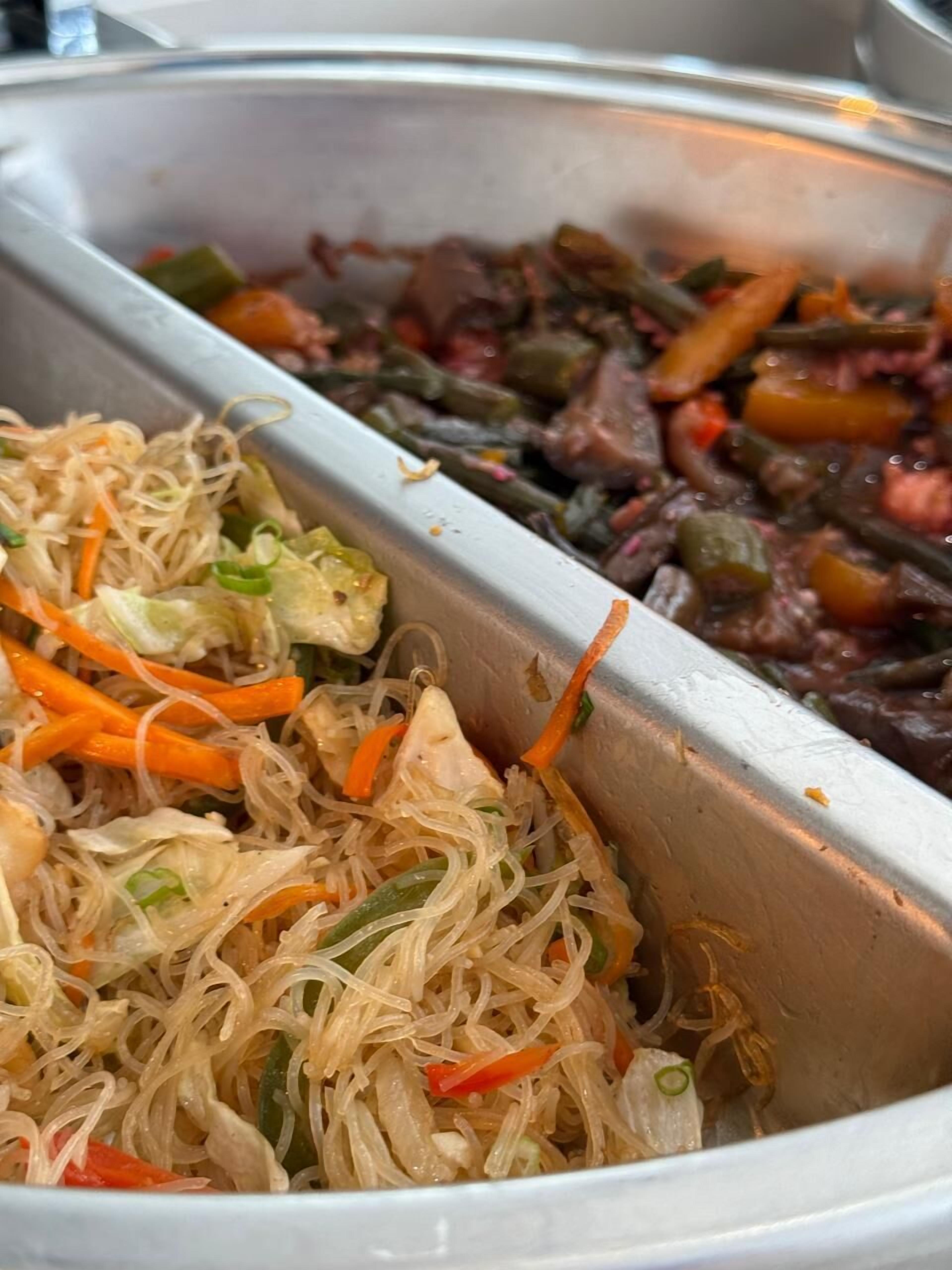 Un bufé con diversos platos, entre ellos fideos, verduras y carne.