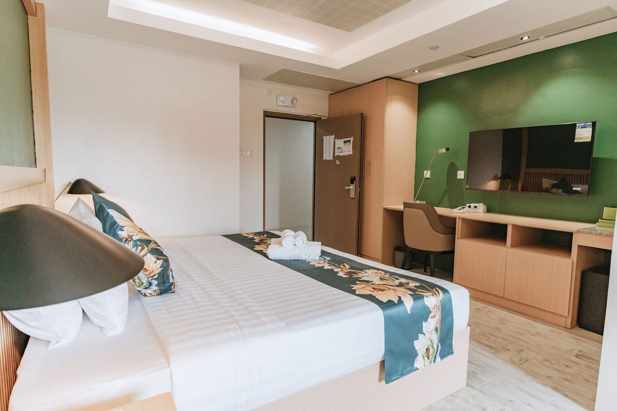 Habitación de hotel con cama, escritorio, silla, espejo y pared verde.