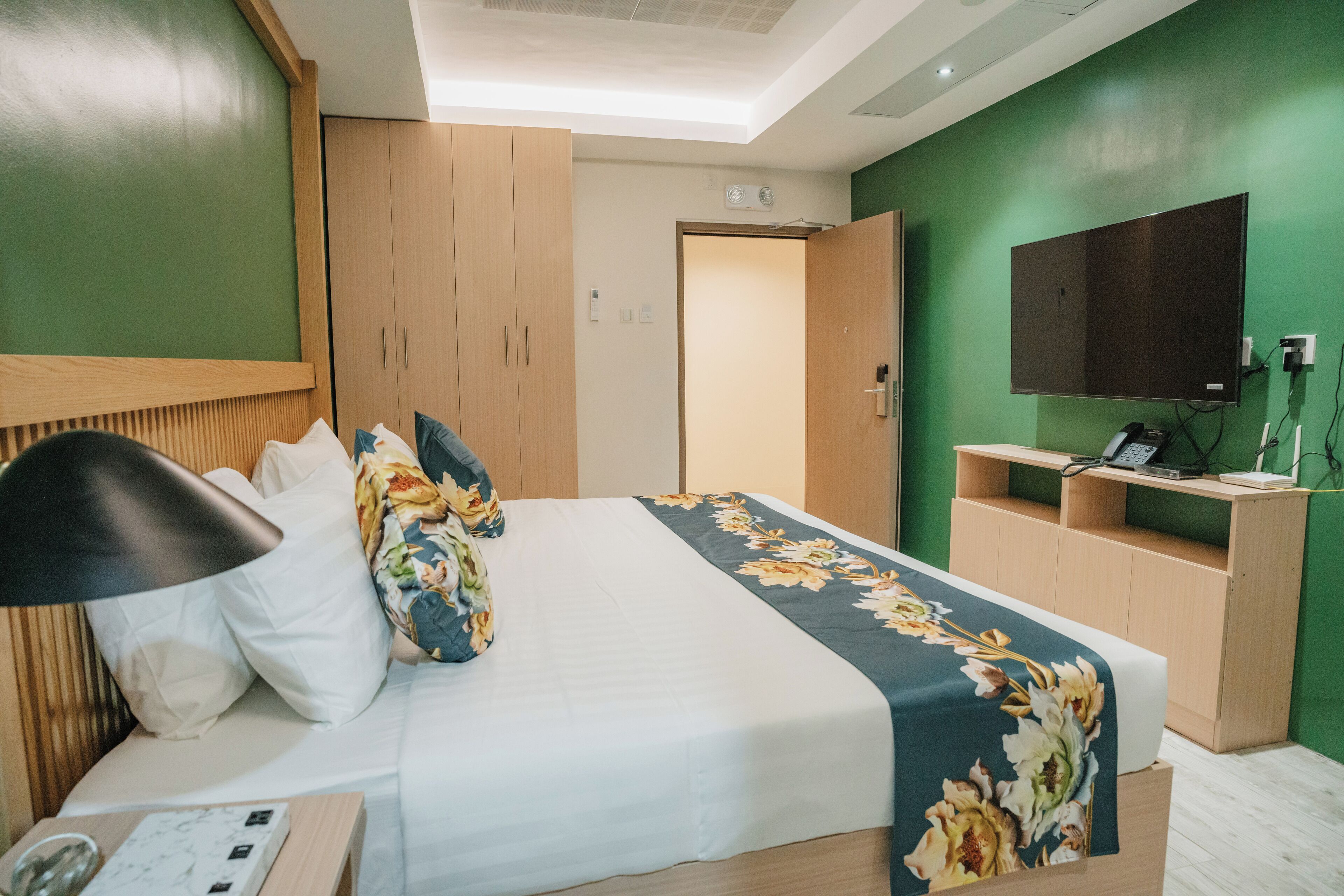 A hotel room with a bed, a desk, a chair, a lamp, and a TV.