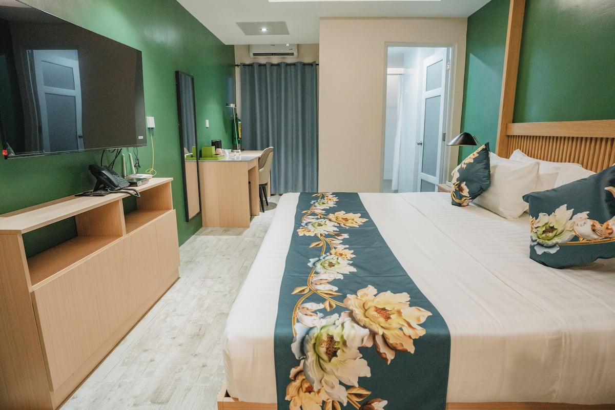 Una habitación de hotel con cama, escritorio, silla, televisor y puerta de baño.