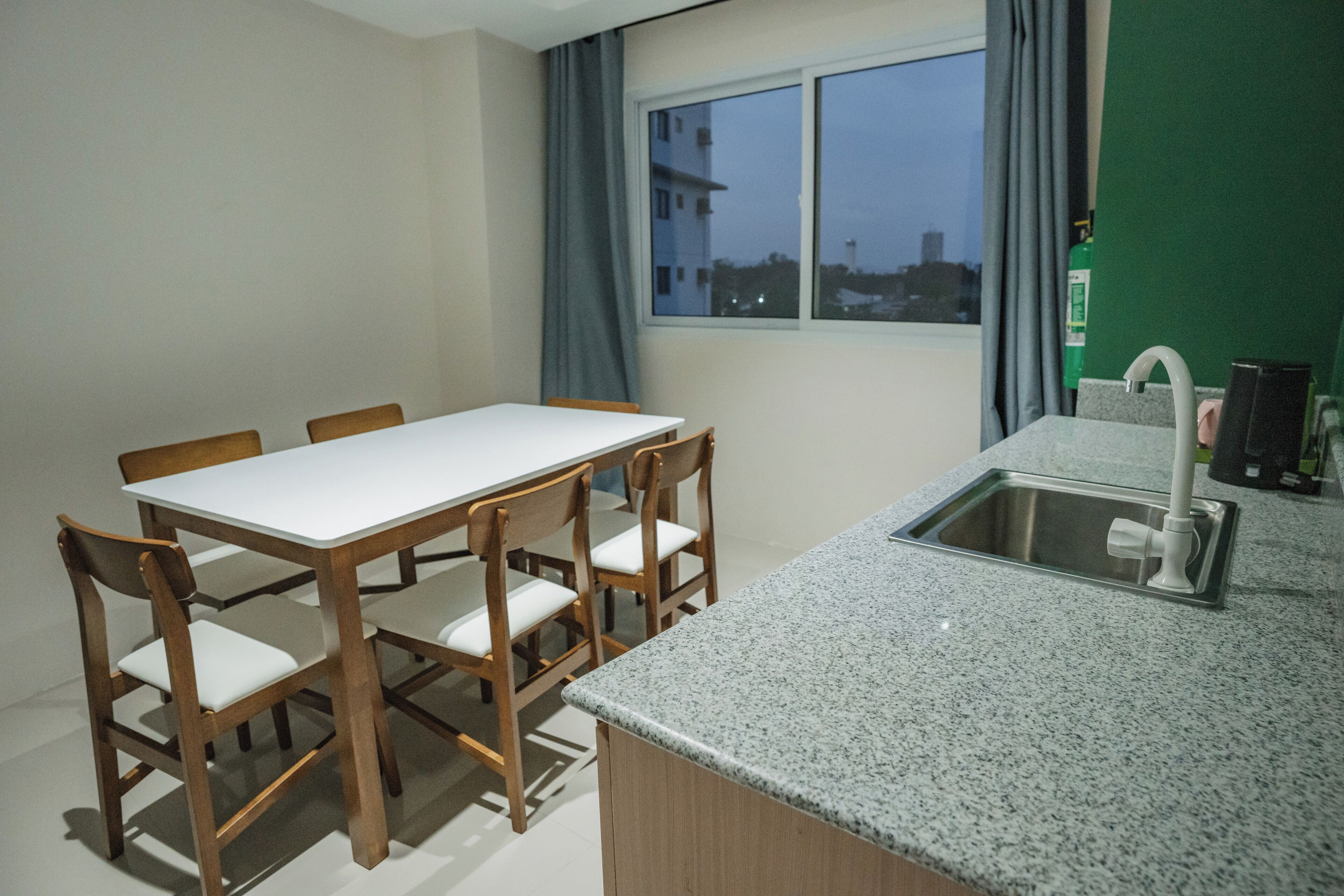 A dining area with a table and chairs, a kitchen with a sink and faucet, and a window with a view of buildings.