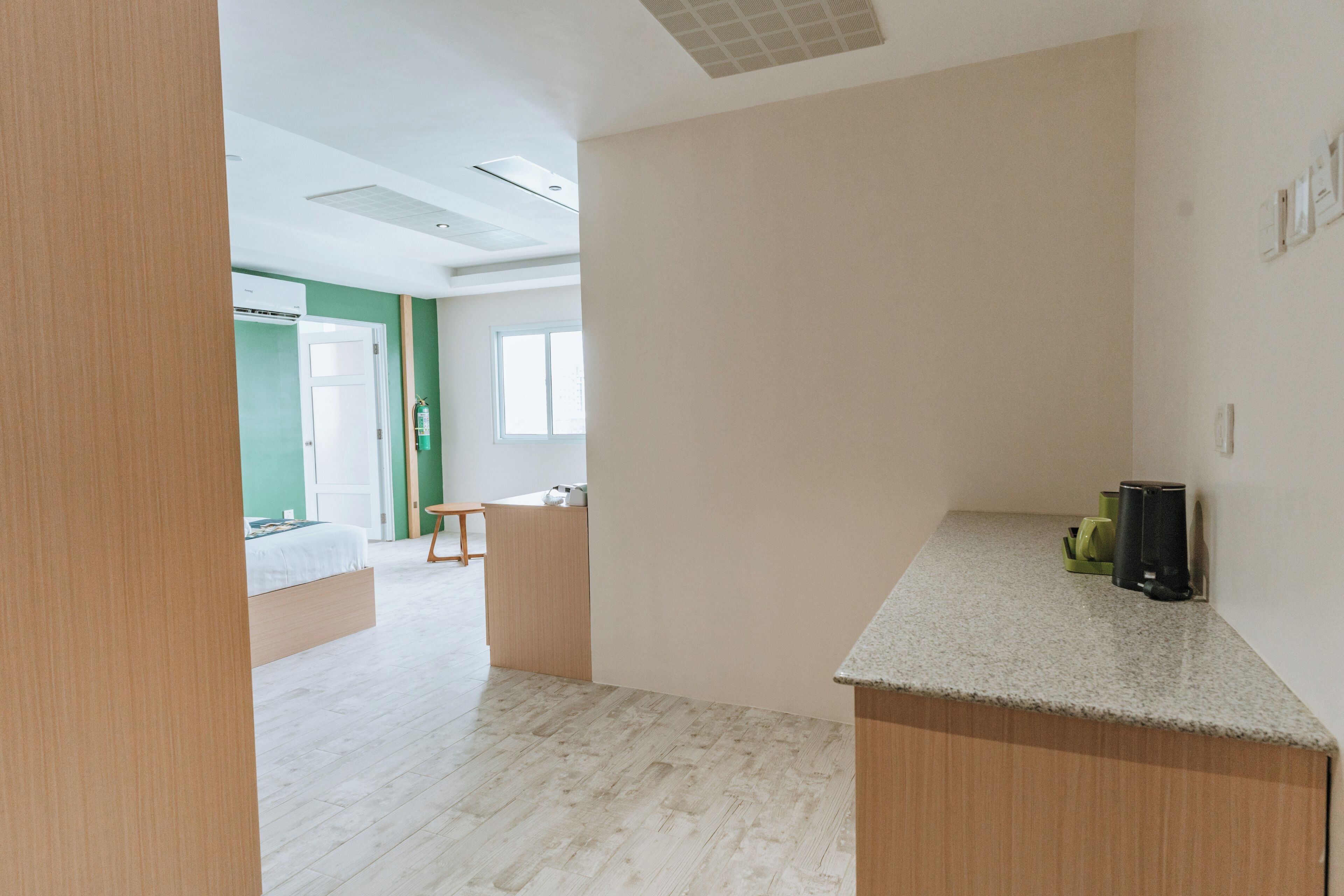 A modern, open-plan room with a kitchenette, a wooden bench, and a large window.
