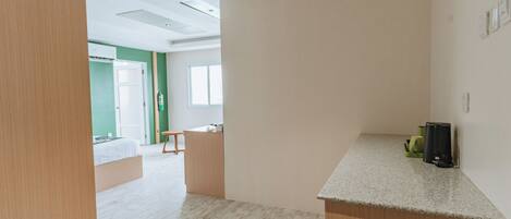 A modern, open-plan room with a kitchenette, a wooden bench, and a large window.