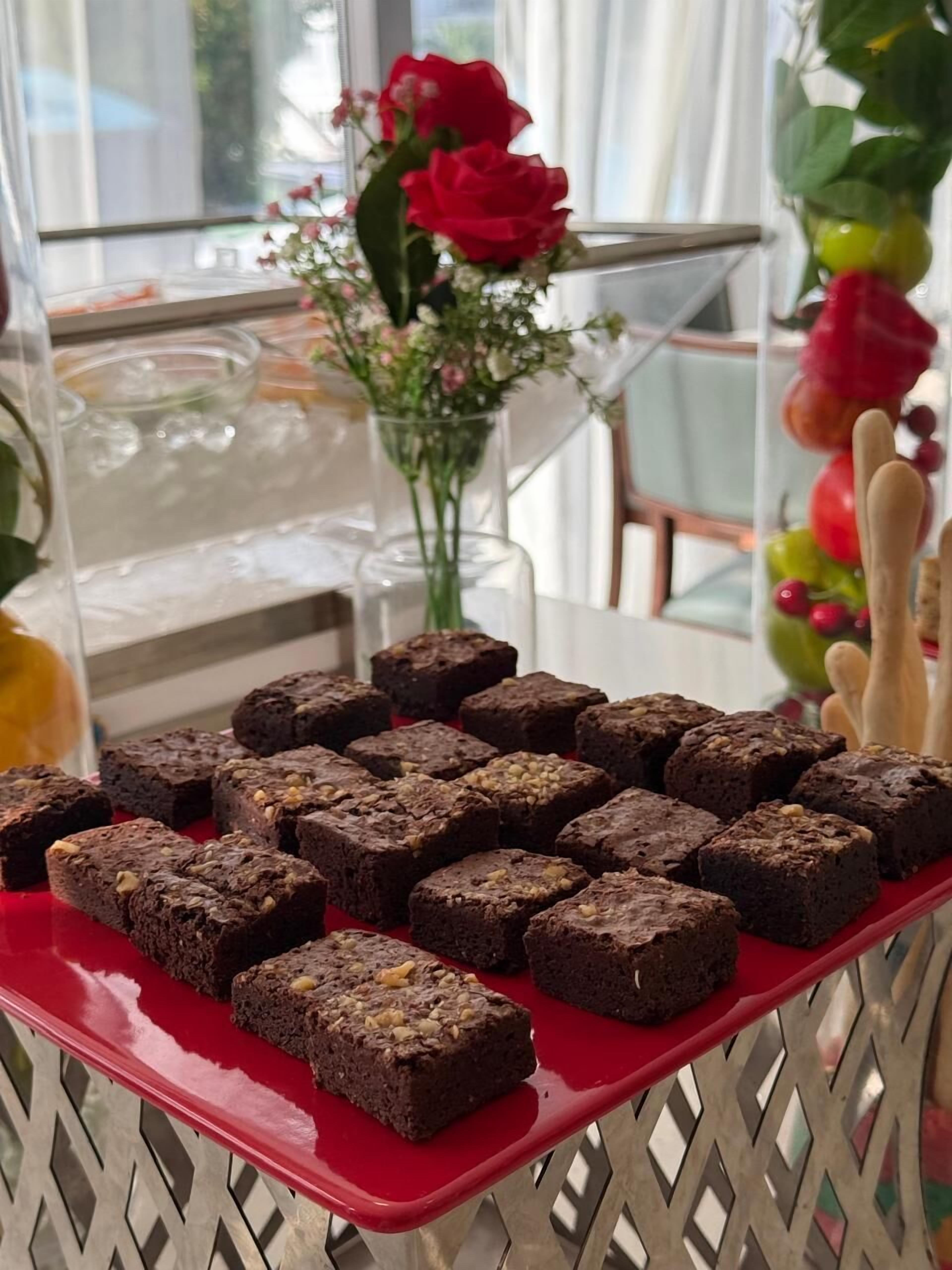 Una mesa con una bandeja de brownies y un florero de flores.