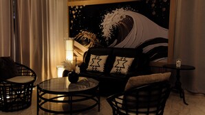 Una habitación con una mesa redonda de vidrio, un sofá con cojines estampados y un cuadro grande con motivos de olas en la pared.