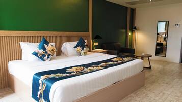 Habitación de hotel con una cama grande, cabecera de madera, pared de acento verde, una mesita con lámpara y un espejo.