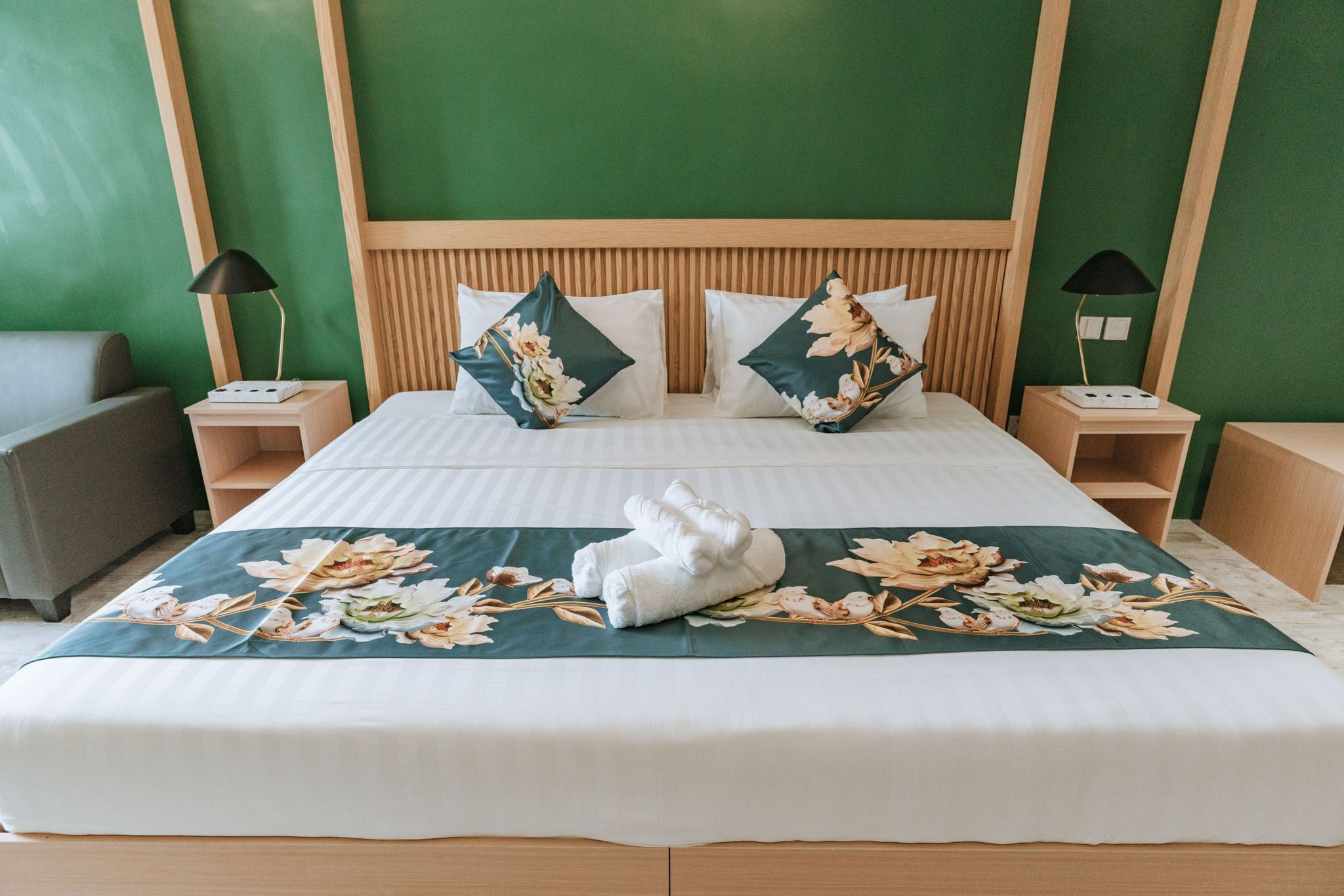 A neatly made bed with floral bedding, two pillows, and a pair of towels.