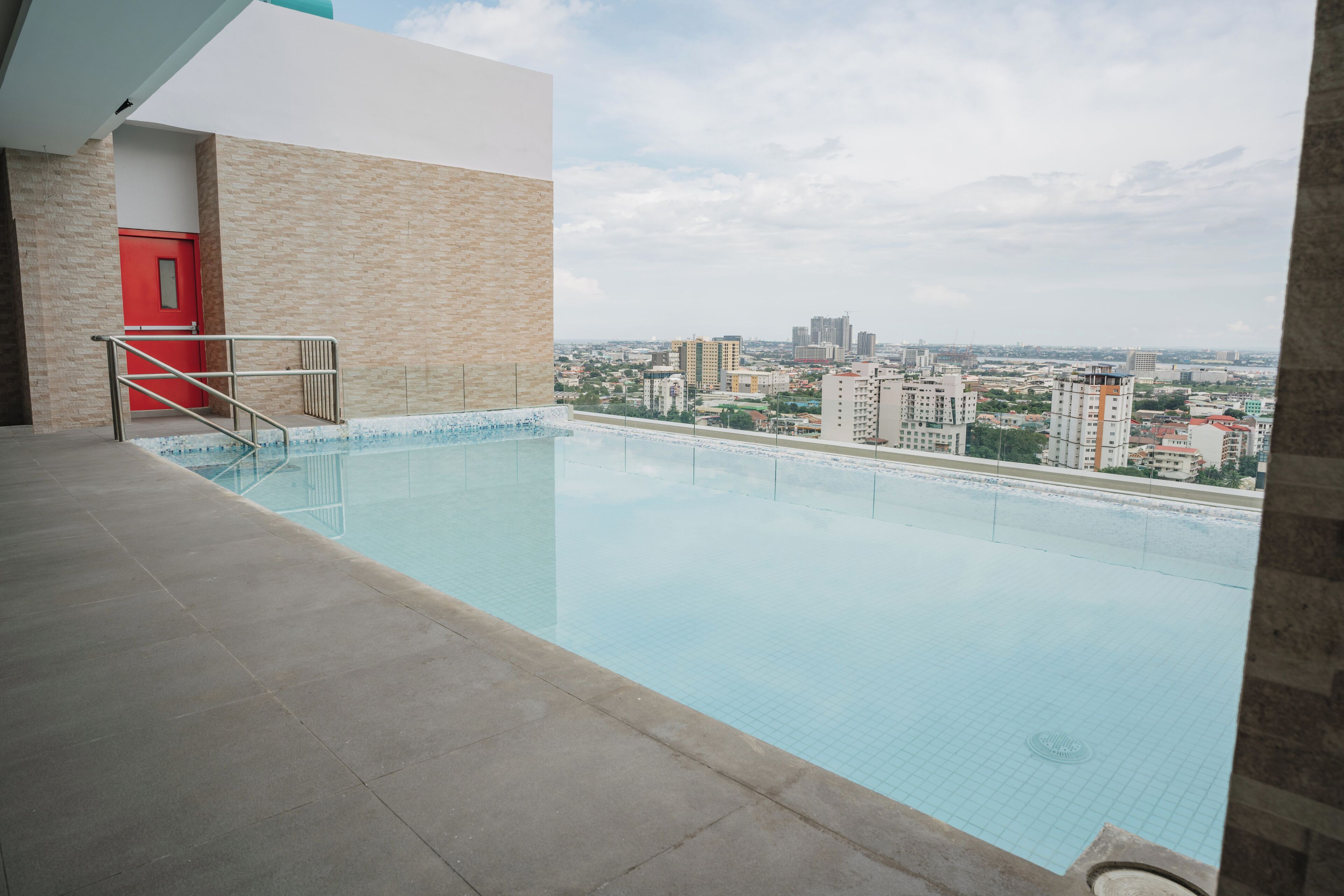 A swimming pool with a city view, a red door, and a tiled floor.