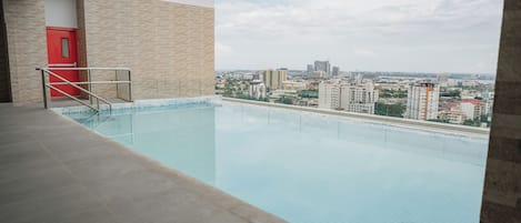 A swimming pool with a city view, a red door, and a tiled floor.