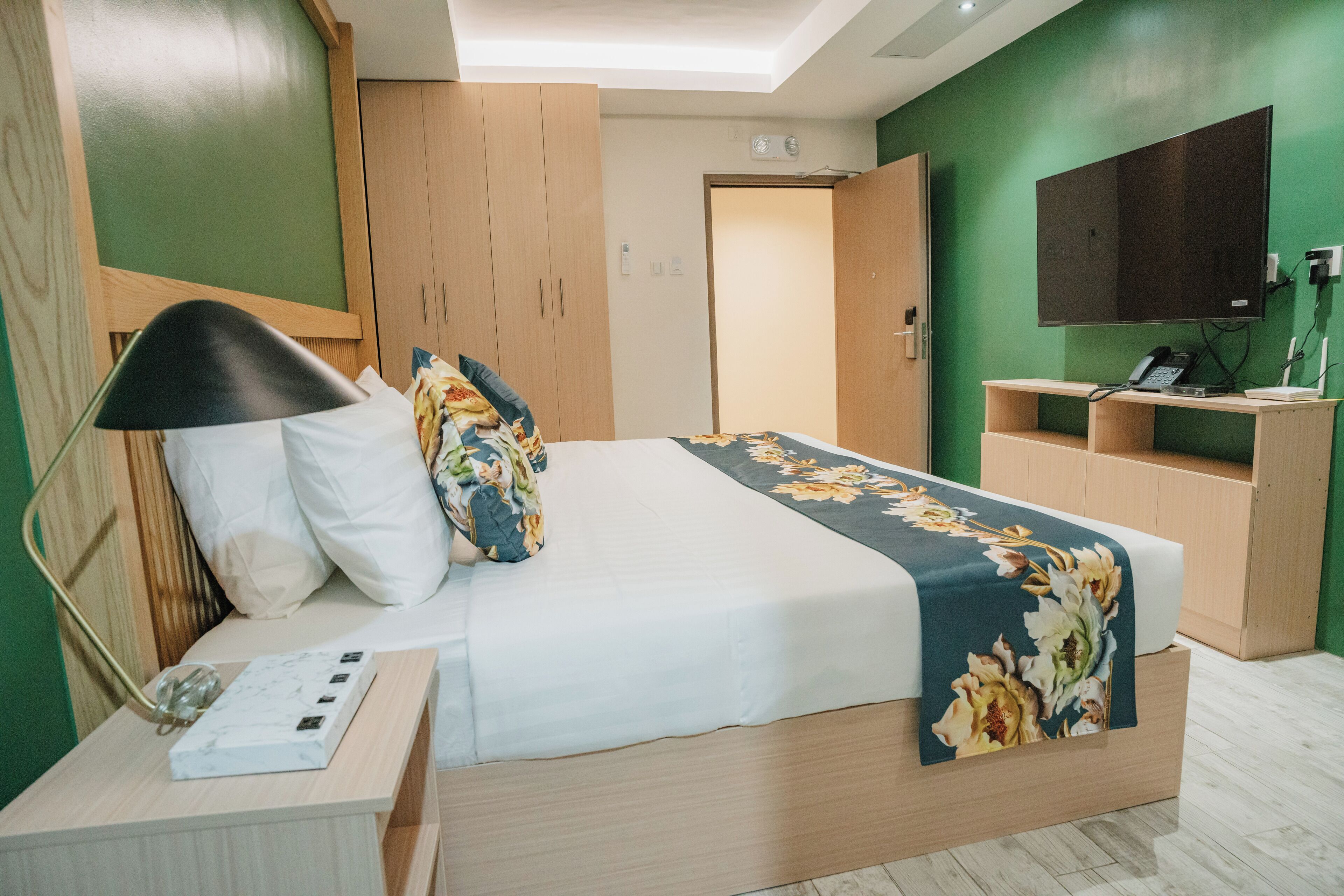 A neatly arranged hotel room with a bed, bedside table, lamp, and a small desk with a telephone.