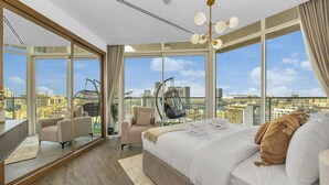 Une chambre moderne avec un grand lit, un fauteuil suspendu et une vue sur la ville grâce à de grandes fenêtres.