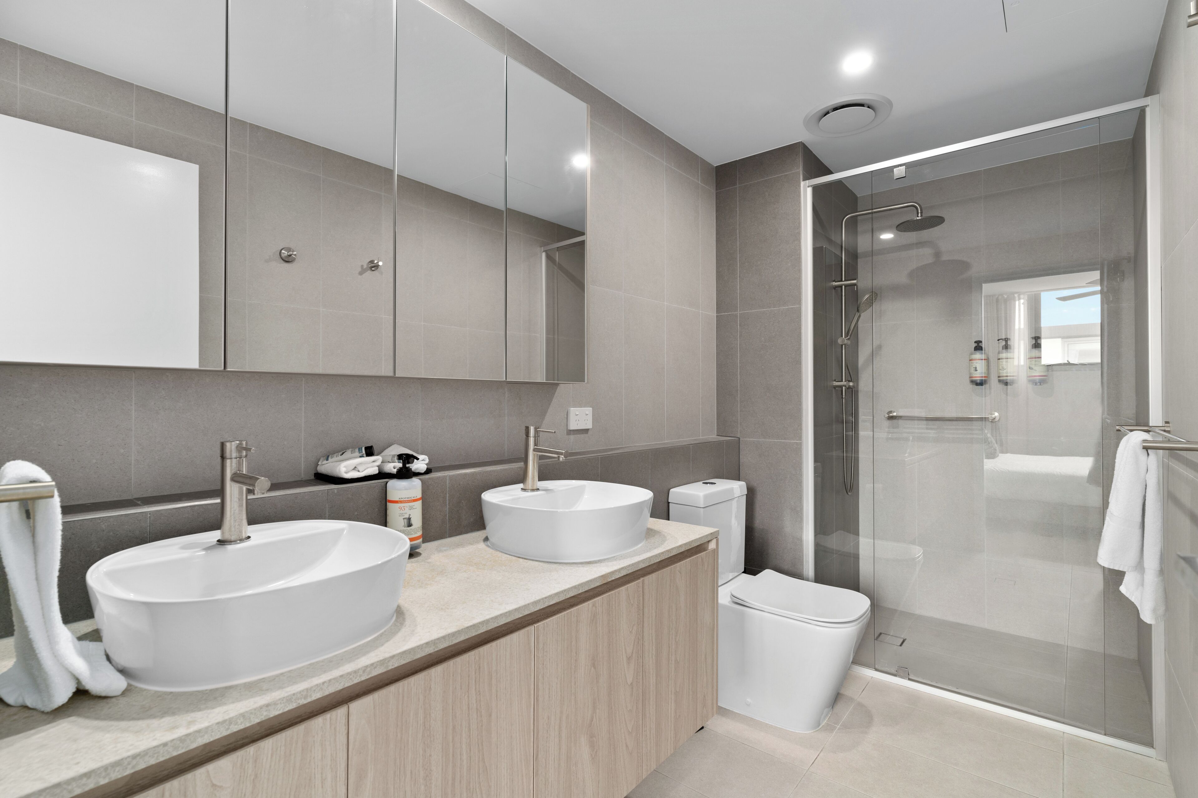 Une salle de bain moderne avec un grand miroir, deux lavabos, des toilettes et une douche à parois de verre.