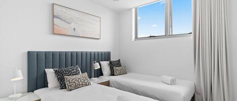 Een hotelkamer met twee bedden, een plafondventilator, een raam met gordijnen en een schilderij aan de muur.