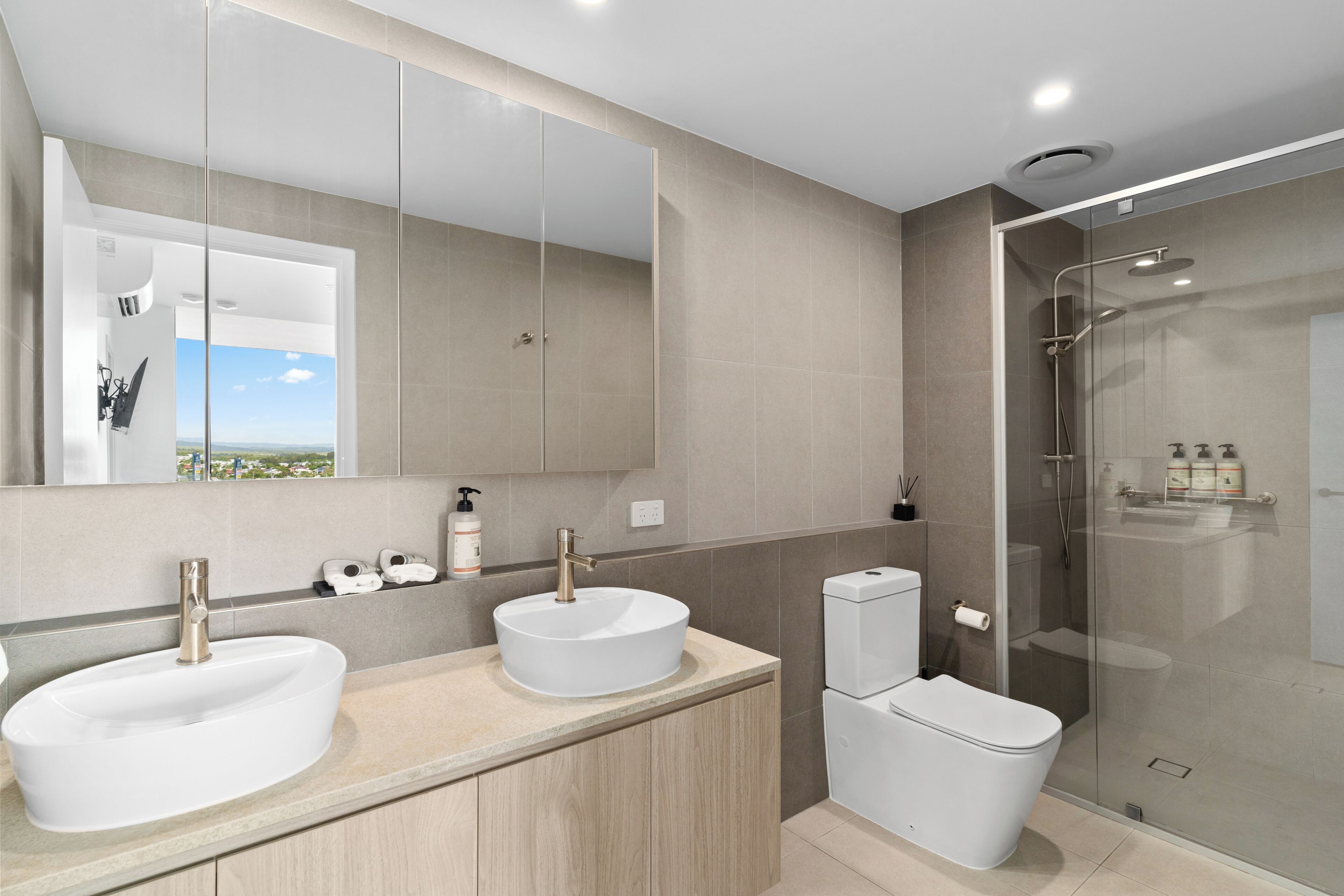 A modern bathroom with two sinks, a toilet, and a glass-enclosed shower.